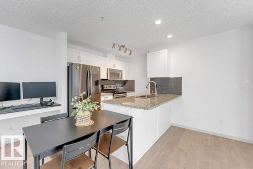 Kitchen featuring stainless steel appliances, granite countertops, white cabinetry, and a dark tile backsplash - #224 390 Windermere Rd Nw, Edmonton, AB 