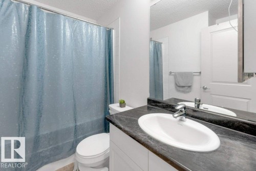 Bathroom featuring a white toilet, built-in vanity with integrated sink, and a dark countertop - #224 390 Windermere Rd Nw, Edmonton, AB 