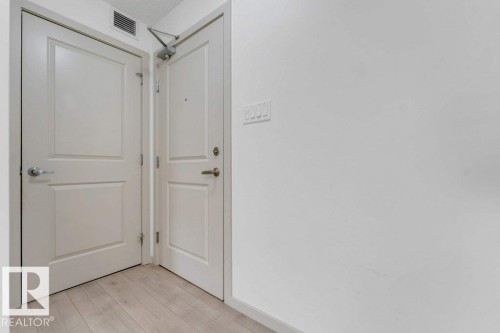 Light wood-finish flooring with white paneled doors and modern door hardware - #224 390 Windermere Rd Nw, Edmonton, AB 