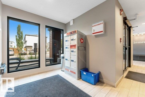 Large storefront windows with black framing, light-toned tile flooring, and integrated parcel lockers - #224 390 Windermere Rd Nw, Edmonton, AB 