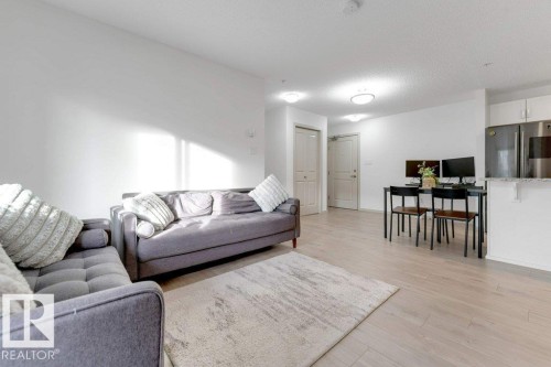 Open-concept living area featuring light wood-finish flooring, recessed lighting, and a kitchen island with seating - #224 390 Windermere Rd Nw, Edmonton, AB 