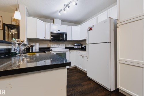 Kitchen with white cabinetry, dark countertops, built-in microwave, and wood-finish flooring - #155 2096 Blackmud Creek Dr Sw, Edmonton, AB 