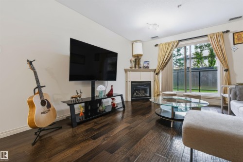 Hardwood-finish flooring, built-in fireplace with mantel, glass sliding door, neutral wall paint, and ceiling-mounted lighting - #155 2096 Blackmud Creek Dr Sw, Edmonton, AB 