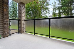 Concrete patio featuring a glass-panel railing with black metal posts, stone veneer accent column, and horizontal siding - 