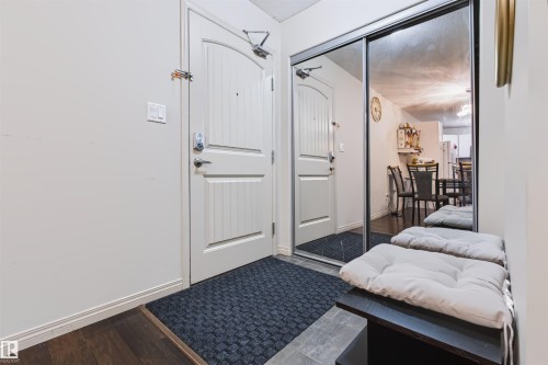 Entryway featuring a paneled door, wood-finish flooring, and a mirrored sliding closet door - #155 2096 Blackmud Creek Dr Sw, Edmonton, AB 