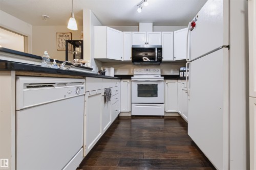 Kitchen featuring white cabinetry, dark countertops, white dishwasher, white electric range, and dark wood-finish flooring - #155 2096 Blackmud Creek Dr Sw, Edmonton, AB 