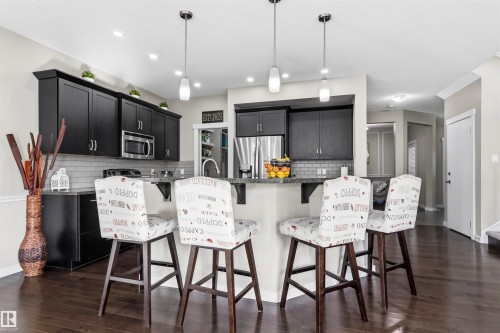 Kitchen featuring dark wood-finish cabinetry, stainless steel appliances, a subway tile backsplash, and a breakfast bar with pendant lighting - 8515 19 Avenue Sw, Edmonton, AB 