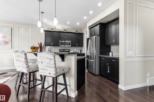 Dark wood-finish flooring, recessed lighting, pendant lighting, stainless steel appliances, and dark cabinetry - 8515 19 Avenue Sw, Edmonton, AB 