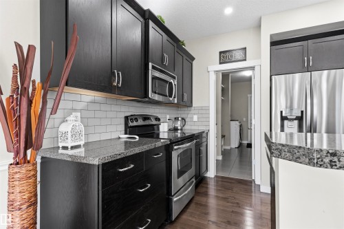Kitchen featuring dark wood-finish cabinetry, stainless steel appliances, granite countertops, and subway tile backsplash - 8515 19 Avenue Sw, Edmonton, AB 