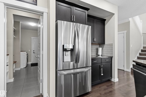 Stainless steel French door refrigerator, dark wood-finish cabinetry, subway tile backsplash, dark granite-style countertop, and dark wood-finish flooring - 8515 19 Avenue Sw, Edmonton, AB 