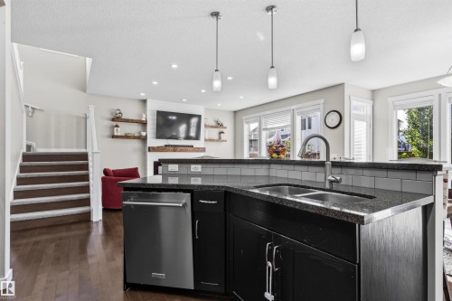 Kitchen island with a double basin sink, dark countertop, and stainless steel dishwasher - 8515 19 Avenue Sw, Edmonton, AB 