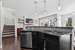 Kitchen island with a double basin sink, dark countertop, and stainless steel dishwasher - 