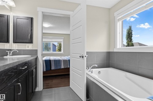 Dual sink vanity with dark wood-finish cabinetry, built-in bathtub, and window with natural light - 8515 19 Avenue Sw, Edmonton, AB 