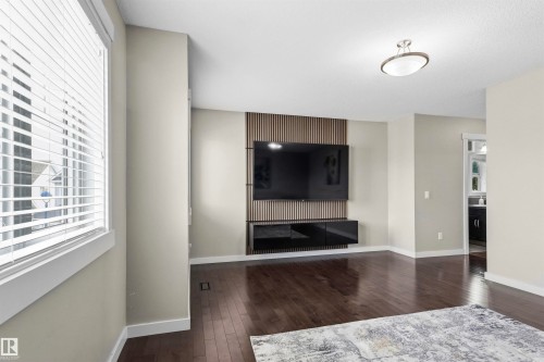 Dark wood-finish flooring, built-in entertainment center with a slatted accent panel, built-in black media console, and a contemporary flush-mount ceiling light - 8515 19 Avenue Sw, Edmonton, AB 