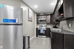 Galley kitchen featuring dark wood-finish cabinetry, stainless steel appliances, and light gray tile flooring - 