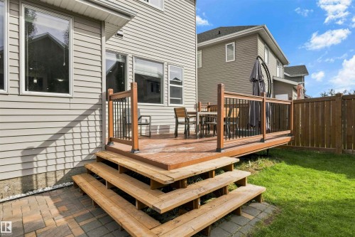 Raised wood-finish deck with black iron balusters, wood-finish stairs, and a paver stone patio - 8515 19 Avenue Sw, Edmonton, AB 