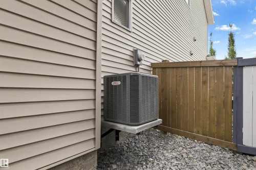 Exterior siding with horizontal panels, a dark-toned air conditioning unit, a wood privacy fence, and a gravel ground cover - 8515 19 Avenue Sw, Edmonton, AB 