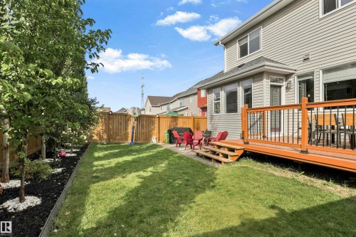 Expansive backyard featuring a wood-tone deck with black balusters, a stone patio, and a manicured lawn - 8515 19 Avenue Sw, Edmonton, AB 