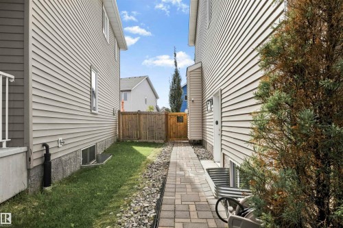 Paved pathway leading to a wooden gate, flanked by siding exteriors and a grass strip - 8515 19 Avenue Sw, Edmonton, AB 