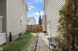 Paved pathway leading to a wooden gate, flanked by siding exteriors and a grass strip - 