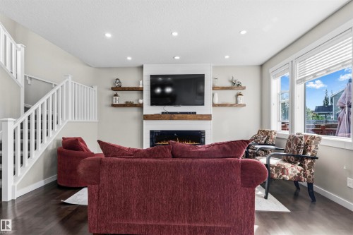 Recessed lighting, wood-finish flooring, white staircase railing, electric fireplace with wood mantel, and large windows - 8515 19 Avenue Sw, Edmonton, AB 