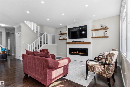 Dark wood-finish flooring, recessed ceiling lighting, electric fireplace with white shiplap surround, wood shelving, and white staircase with spindles - 8515 19 Avenue Sw, Edmonton, AB 