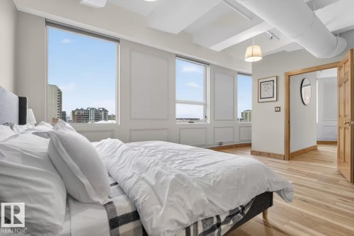 High ceilings with exposed ductwork, large windows providing abundant natural light, light wood-finish flooring, and a natural wood-finish door frame - #501 10105 109 St Nw, Edmonton, AB 