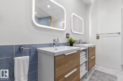 Dual floating vanities with integrated sinks, illuminated mirrors, wood-finish cabinetry, and blue subway tile wainscoting - 