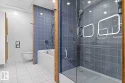 Bathroom featuring a glass-enclosed shower, a built-in tub, blue wall tile, white floor tile, and a wall-mounted toilet - 