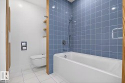 White bathtub with chrome fixtures, blue subway tile surround, and a wall-mounted toilet - 