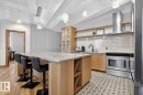Expansive kitchen island with a light-toned countertop, natural wood-finish cabinetry, stainless steel oven, white subway tile backsplash, and decorative floor tiling - #501 10105 109 St Nw, Edmonton, AB 