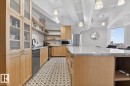 Expansive kitchen island with a stone countertop, light wood cabinetry, patterned floor tiling, exposed ceiling ductwork, and pendant lighting fixtures - #501 10105 109 St Nw, Edmonton, AB 