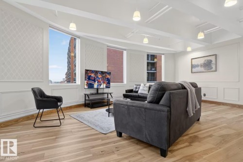 Spacious interior featuring wood-finish flooring, large windows, decorative wall paneling, and an intricate ceiling design with recessed lighting - #501 10105 109 St Nw, Edmonton, AB 