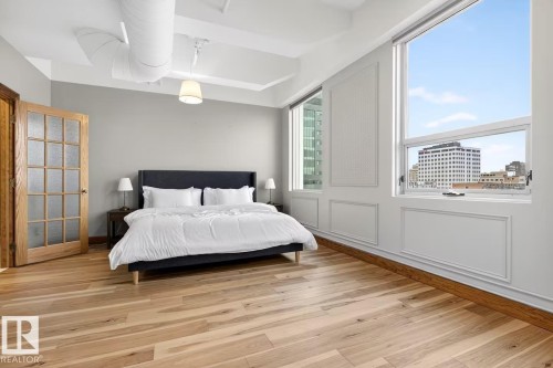 Hardwood flooring, exposed ceiling ductwork, high ceilings, large windows, and a wood-frame door with frosted glass panels - #501 10105 109 St Nw, Edmonton, AB 