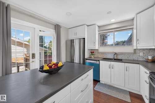 White shaker cabinetry, stainless steel refrigerator, dark countertops, tile backsplash, and wood-finish flooring - 7704 13 Avenue Nw, Edmonton, AB 
