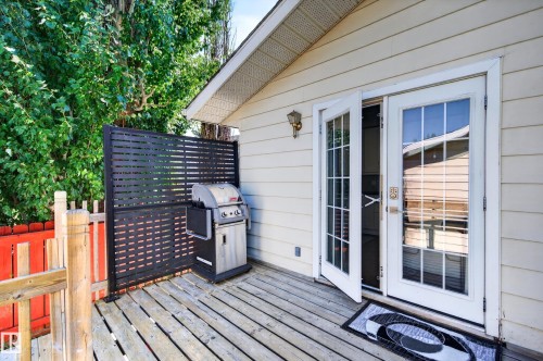 Wooden deck with horizontal privacy screen, white French doors with glass panes, and beige siding - 7704 13 Avenue Nw, Edmonton, AB 