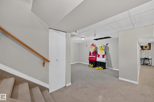 Carpeted stairs with a wood handrail, leading to a carpeted lower level with a drop ceiling - 7704 13 Avenue Nw, Edmonton, AB 