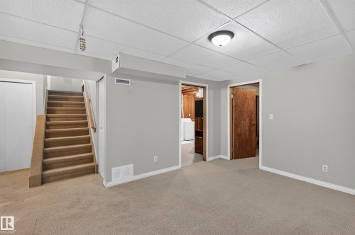 Carpeted flooring, light gray wall paint, drop ceiling with recessed lighting, wood-finish interior doors, and a carpeted staircase - 7704 13 Avenue Nw, Edmonton, AB 