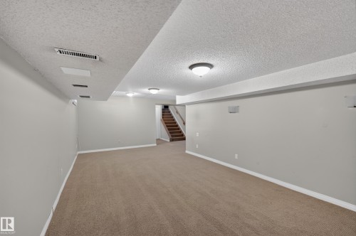 Carpeted flooring, light gray wall paint, recessed lighting, surface-mounted lighting, and a visible staircase with wood treads - 7704 13 Avenue Nw, Edmonton, AB 