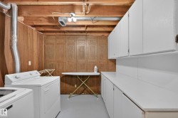 Laundry area featuring wood paneling, open ceiling joists, white cabinetry, and a white countertop - 