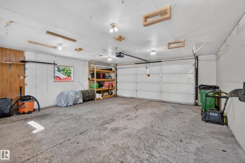 Attached garage with a roll-up door, built-in shelving, and multiple overhead light fixtures - 7704 13 Avenue Nw, Edmonton, AB 