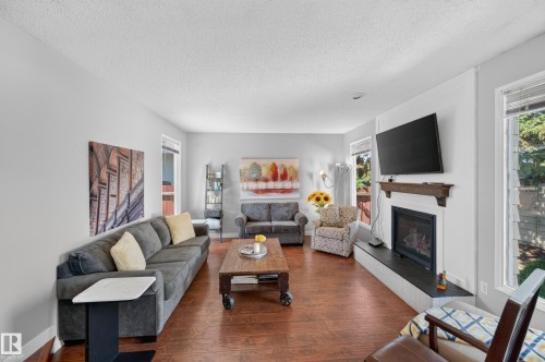 Spacious living area featuring wood-finish flooring, a built-in fireplace with a dark mantel, and multiple windows - 7704 13 Avenue Nw, Edmonton, AB 