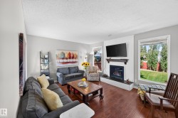 Hardwood-finish flooring, recessed fireplace with a dark mantel, large windows with white trim, and a built-in bookshelf - 