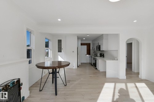 Open-concept living area with wood-finish flooring, white cabinetry, integrated kitchen appliances, and arched doorway - 11914 124 Street Nw, Edmonton, AB 