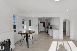 Open-concept living area with wood-finish flooring, white cabinetry, integrated kitchen appliances, and arched doorway - 