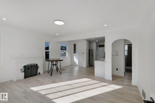 Light wood-finish flooring, recessed lighting, and a white-painted fireplace with decorative tile accents - 11914 124 Street Nw, Edmonton, AB 