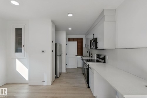 Galley kitchen featuring white cabinetry, stainless steel appliances, light-toned wood-finish flooring, and recessed lighting - 11914 124 Street Nw, Edmonton, AB 