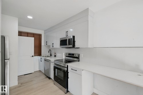 Kitchen with light wood-finish flooring, white cabinetry, stainless steel appliances, and a black gooseneck faucet - 11914 124 Street Nw, Edmonton, AB 
