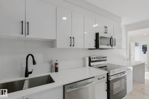 White cabinetry with matte black hardware, stainless steel appliances, dual basin sink with gooseneck faucet, light-toned flooring, and white countertops - 11914 124 Street Nw, Edmonton, AB 