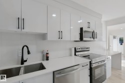 White cabinetry with matte black hardware, stainless steel appliances, dual basin sink with gooseneck faucet, light-toned flooring, and white countertops - 